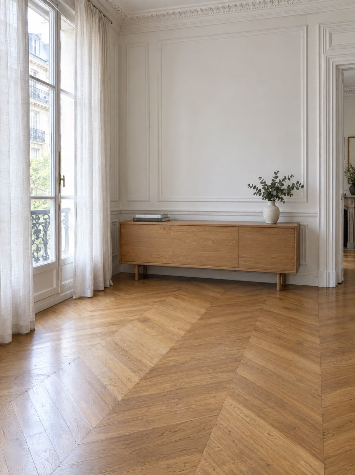 A bright Parisian living room with chevron parquet and an oak sideboard, without an armchair